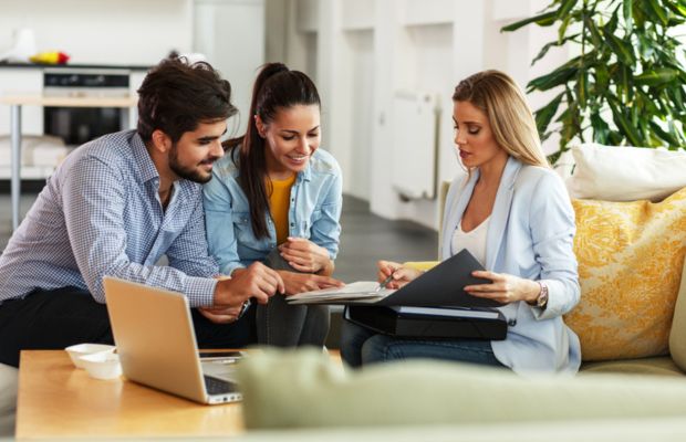 Three people discussing documents on a sofa