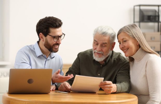 Three people discussing documents at a table Laptop present
