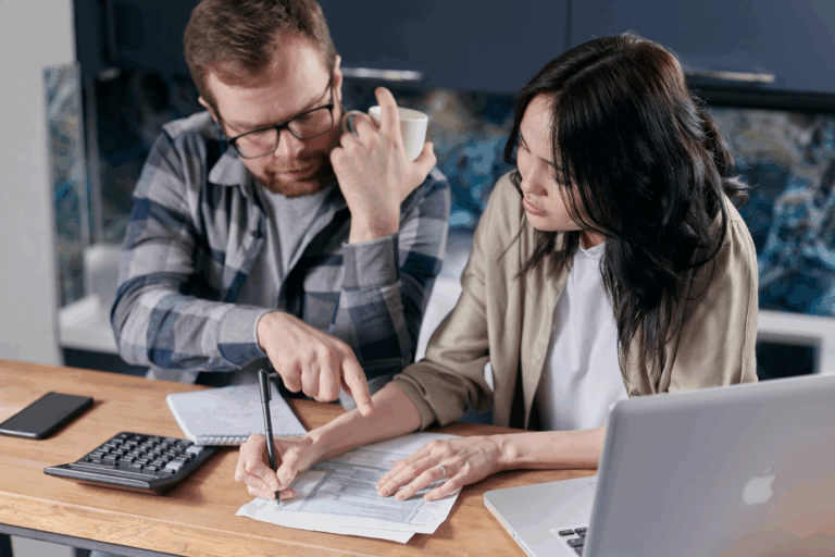 A couple sitting at a kitchen table, reviewing financial documents with a calculator and laptop ,representing personal tax planning.