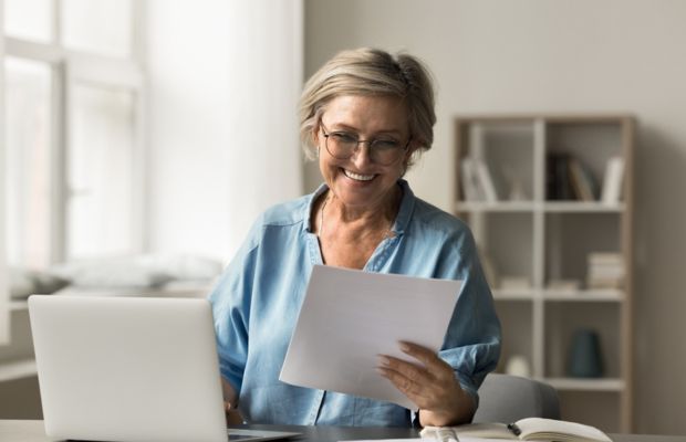 Smiling woman reading paper near laptop in a Bright room