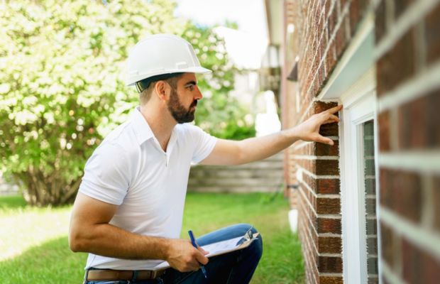 Man inspecting brick wall near window wearing hard hat