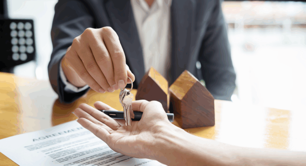 Close-up of estate agent handing house keys to a buyer over a signed agreement, symbolising a successful autumn property sale before Christmas