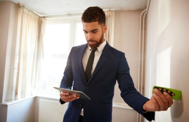 Man in suit holding tablet and measuring device indoors