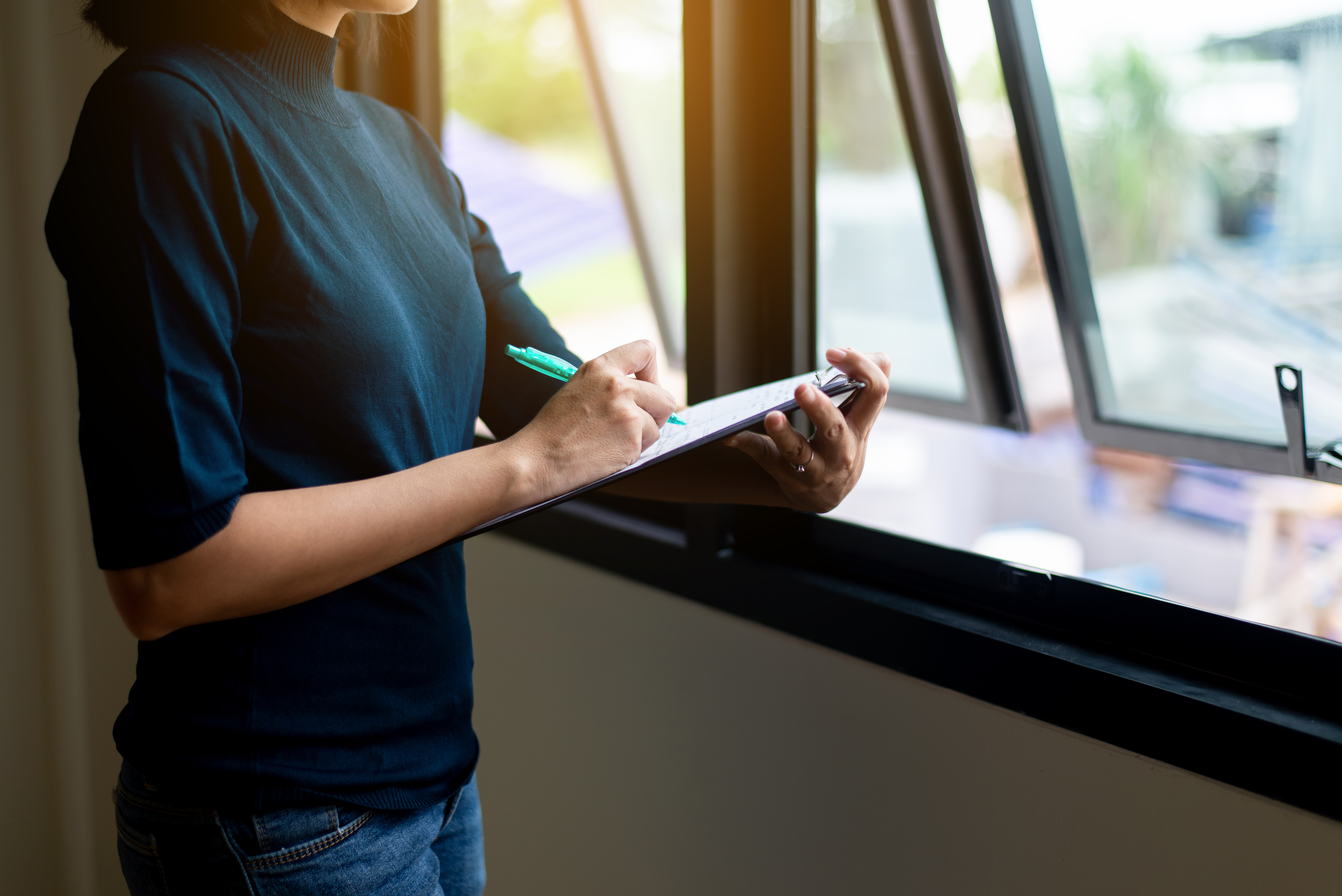 Landlord inspecting a rental property window and taking notes on a clipboard during a mid-tenancy inspection in Solihull.