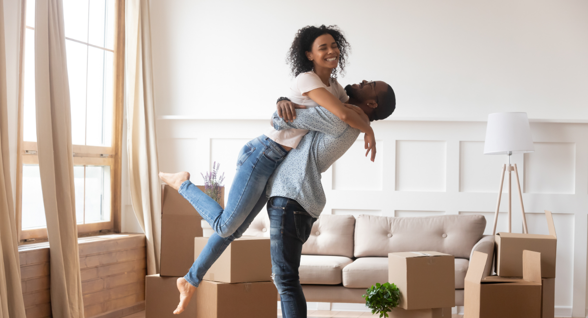 Smiling couple celebrating while unpacking moving boxes inside a modern living room, representing Martin & Co’s 2025 guide to what buyers want in Solihull.