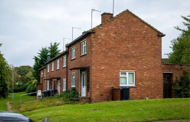 Two story brick house with green lawn and garbage bins