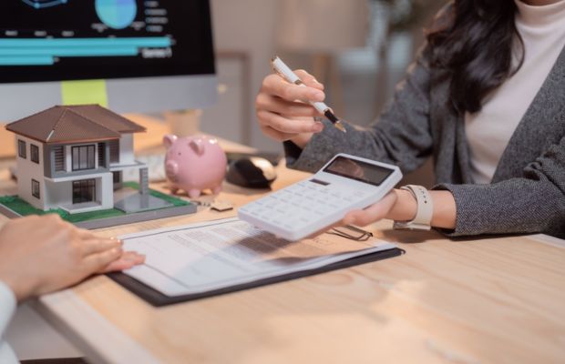 Calculator, house model, piggy bank, documents on table.