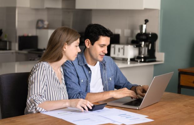 A man and woman sit at a table, focused on a laptop, engaged in discussion or collaboration.
