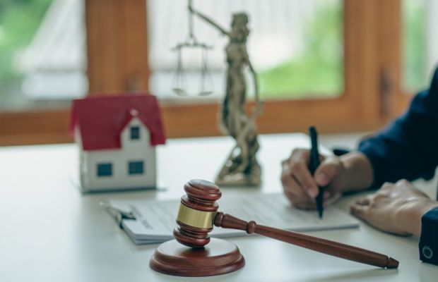 Gavel, scales of justice, house model, documents, writing hand.