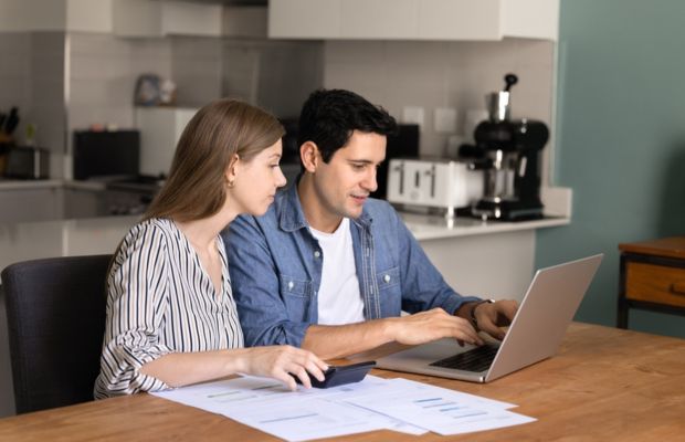A man and woman sit at a table, collaborating on a laptop, engaged in discussion.