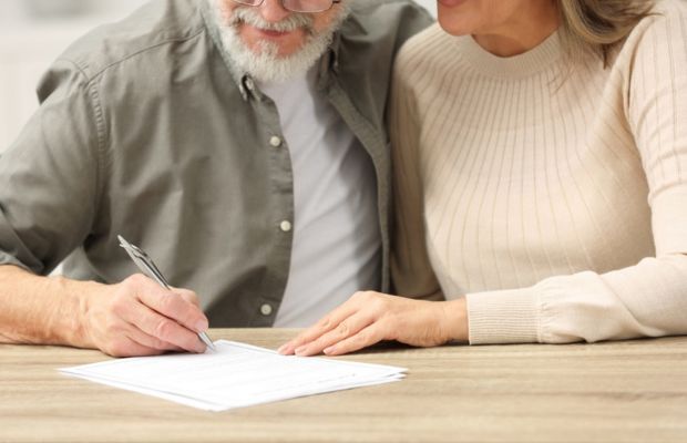 An elderly couple collaboratively signing an important document at a table.