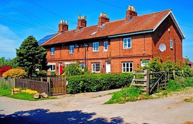 Brick house with garden and fence, clear blue sky.