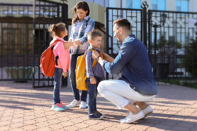 Parents helping children with backpacks outside a school, preparing for the school day