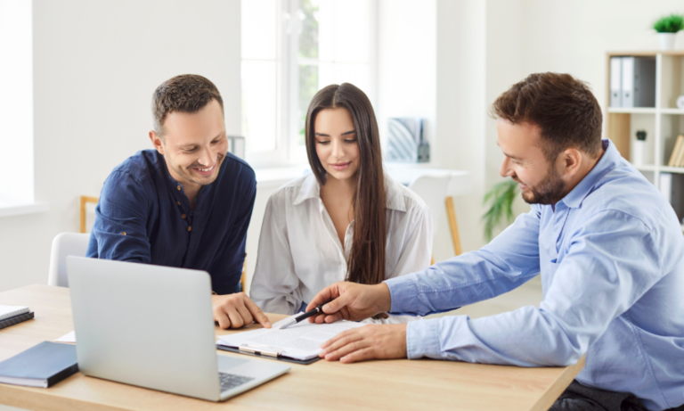 Couple reviewing rental agreement with letting agent at table with laptop and documents