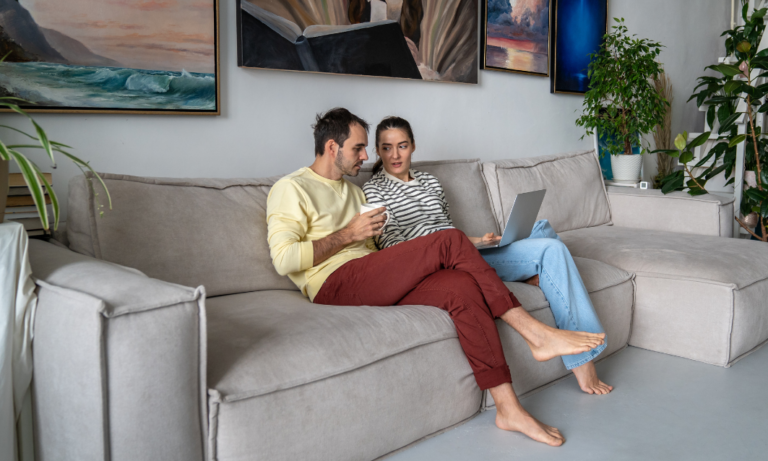 Couple sitting on a sofa reviewing rental property details on a laptop in a modern living room