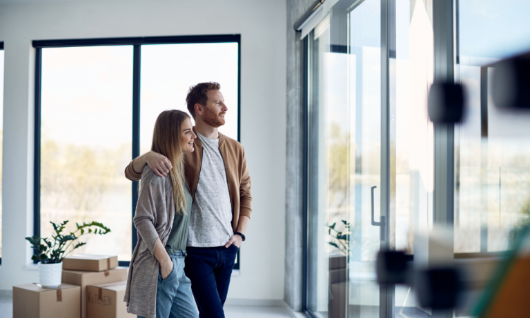 Couple standing inside a bright modern home looking out through large windows during a property viewing