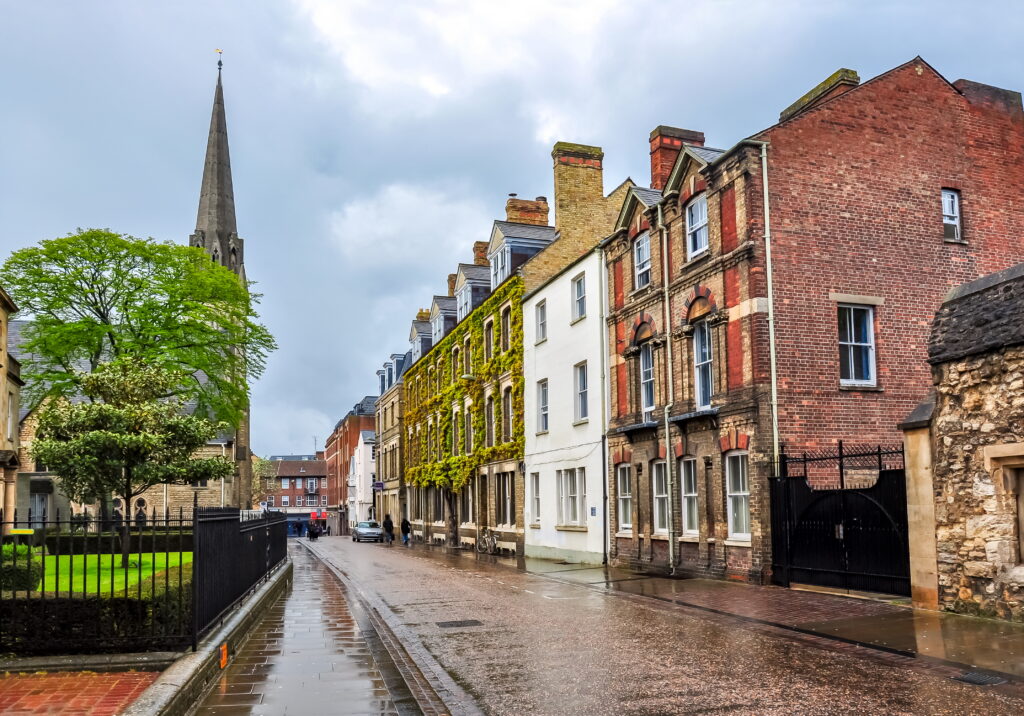 Historic residential street in Oxford with traditional homes and church spire near popular rental areas.