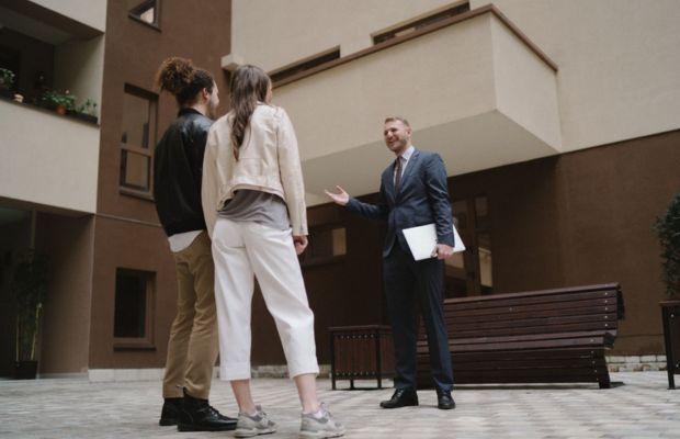 A man and two women stand together in front of a modern building, smiling and engaged in conversation.