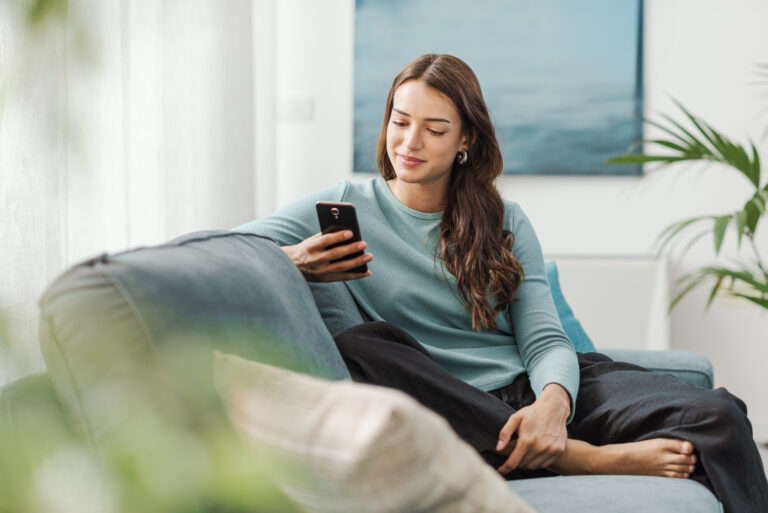 A prospective homebuyer using her phone while relaxing in a modern living room in Dunfermline.
