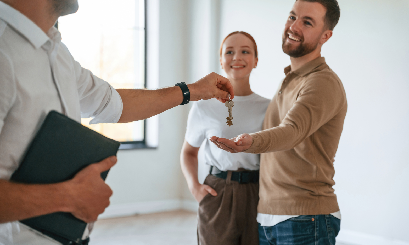 An estate agent handing house keys to a smiling couple inside a bright Chelmsford property.