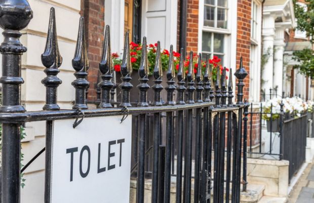 Toilet sign displayed on a fence in front of a building, indicating restroom location for visitors.