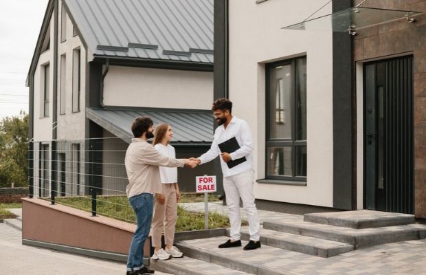 A couple shaking hands in front of a house, symbolizing a successful agreement or partnership.