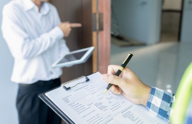 A man writes on a clipboard while another man stands behind him, observing the task being performed.
