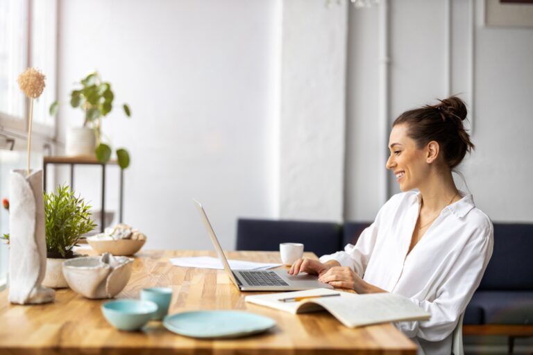 Smiling woman researching property on a laptop at a wooden dining table, representing buyers and renters in Harborne B17