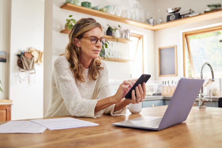 Landlord using a phone and laptop at a kitchen counter to check Housing (Scotland) Act changes for an Ayr rental