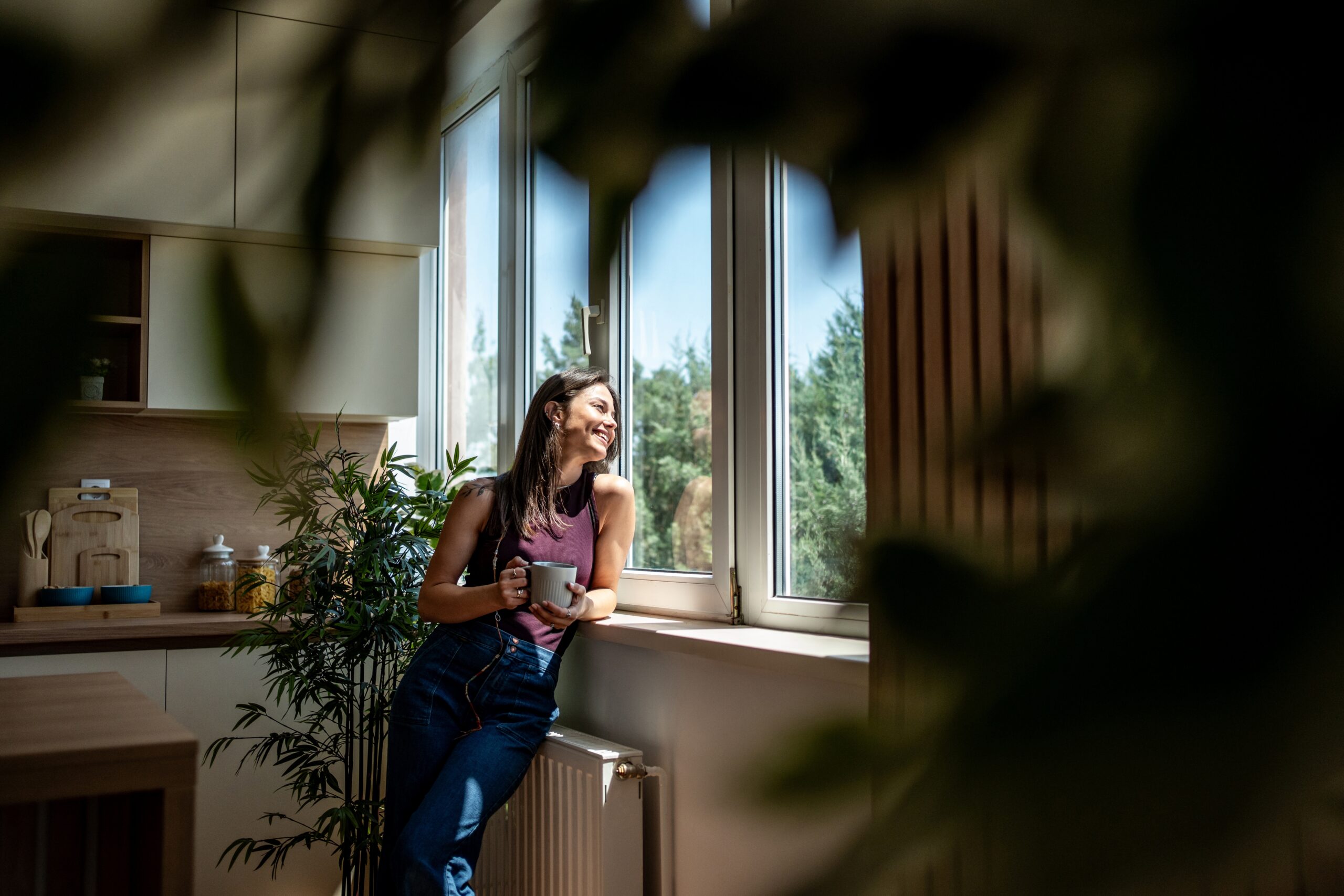 Woman with a mug standing by a large window in a bright kitchen, representing living in TN4 around Southborough and Rusthall
